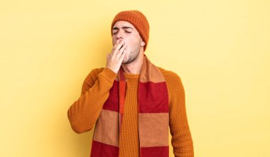 Genç yakışıklı adam tembelce esniyor, uykulu, yorgun ve sıkkın görünüyor.