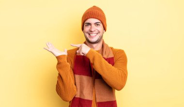 Genç yakışıklı adam neşeyle gülümsüyor ve bir objeyi göstererek veya reklamını yaparak avucundaki fotokopi alanını gösteriyor.