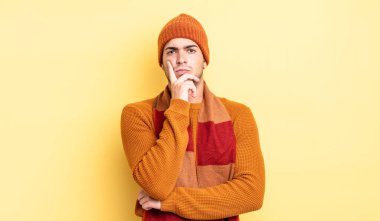 Genç yakışıklı adam ciddi, düşünceli ve güvensiz görünüyor, bir kolu çapraz ve çene üzerinde, seçenekleri tartıyor