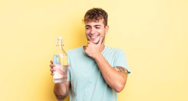 Genç ve yakışıklı bir adam mutlu ve kendinden emin bir ifadeyle gülümsüyor, elleri çenesinde. su kavramı