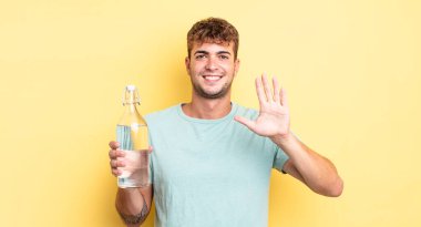 Genç yakışıklı adam gülümsüyor ve arkadaş canlısı görünüyor, beş numarayı gösteriyor. su kavramı