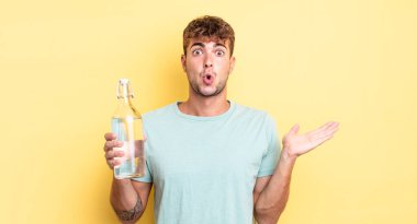 Genç, yakışıklı adam şaşırmış ve şok olmuş görünüyor. Çenesi düşmüş, elinde bir nesne var. su kavramı