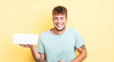 Genç yakışıklı bir adam komik bir şakaya yüksek sesle gülüyor. beyaz kutu kavramı