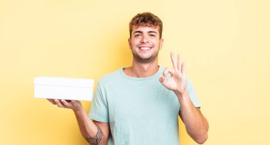 Genç yakışıklı adam kendini mutlu hissediyor, iyi bir jestle onaylıyor. beyaz kutu kavramı