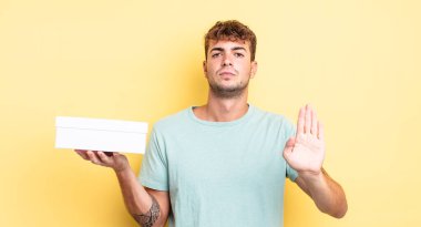 Genç ve yakışıklı adam ciddi görünüyor. Avuç içi gösteriyor. Durdurma hareketi yapıyor. beyaz kutu kavramı