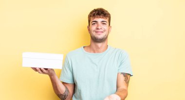 Genç ve yakışıklı bir adam arkadaşça gülümsüyor ve bir konsept sunuyor. beyaz kutu kavramı