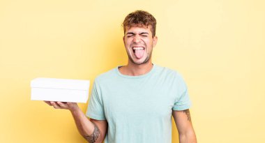 Genç, yakışıklı, neşeli ve asi tavırlı, şaka yapan ve dilini dışarı çıkaran bir adam. beyaz kutu kavramı