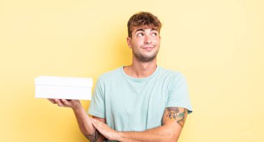 Genç yakışıklı adam omuz silkiyor, kafası karışık ve kararsız. beyaz kutu kavramı