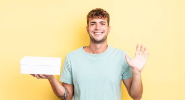 Genç yakışıklı adam mutlu bir şekilde gülümsüyor, el sallıyor, sizi selamlıyor ve selamlıyor. beyaz kutu kavramı