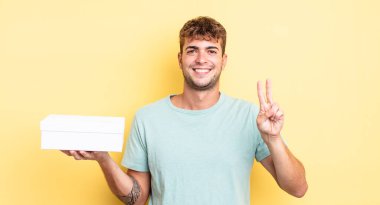 Genç yakışıklı adam gülümsüyor ve arkadaş canlısı görünüyor, iki numarayı gösteriyor. beyaz kutu kavramı