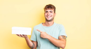 Genç yakışıklı adam neşeyle gülümsüyor, mutlu hissediyor ve bir tarafı işaret ediyor. beyaz kutu kavramı