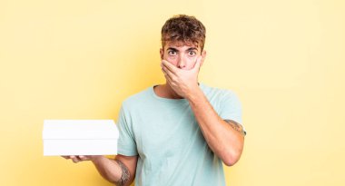 Genç ve yakışıklı bir adam elleri ile ağzını kapatıyor ve şok geçiriyor. beyaz kutu kavramı