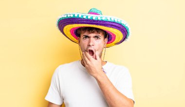 Ağzı ve gözleri açık ve eli çenesinde genç yakışıklı bir adam. Meksika şapkası konsepti