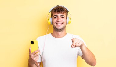 Genç ve yakışıklı bir adam kamerayı işaret ederek seni seçiyor. kulaklıklar ve akıllı telefon konsepti