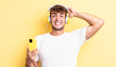 Genç ve yakışıklı bir adam stresli, endişeli ya da korkmuş hissediyor. Elleri başının üstünde. kulaklıklar ve akıllı telefon konsepti