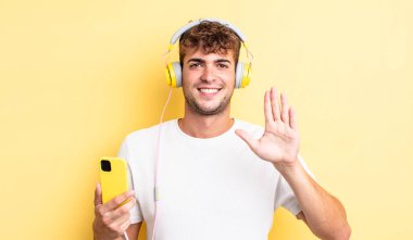 Genç yakışıklı adam gülümsüyor ve arkadaş canlısı görünüyor, beş numarayı gösteriyor. kulaklıklar ve akıllı telefon konsepti