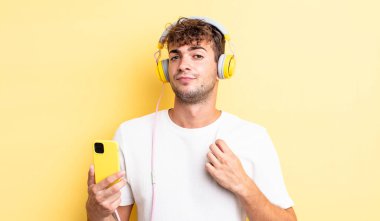 Genç yakışıklı adam kibirli, başarılı, pozitif ve gururlu görünüyor. kulaklıklar ve akıllı telefon konsepti