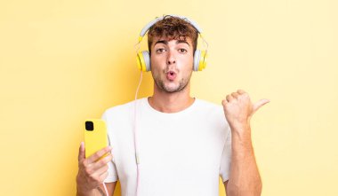 İnanamadığı için şaşırmış genç ve yakışıklı bir adam. kulaklıklar ve akıllı telefon konsepti