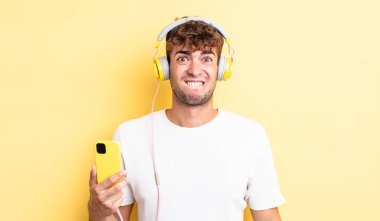 Kafası karışmış ve kafası karışmış genç yakışıklı bir adam. kulaklıklar ve akıllı telefon konsepti