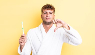 Genç ve yakışıklı bir adam kendini kötü hissediyor, baş parmağını kaldırıyor. diş fırçası kavramı