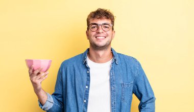 Genç yakışıklı adam mutlu bir şekilde gülümsüyor, eli kalçasında ve kendinden emin. boş kase kavramı