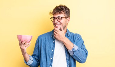 Genç ve yakışıklı bir adam mutlu ve kendinden emin bir ifadeyle gülümsüyor, elleri çenesinde. boş kase kavramı