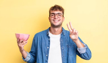 Genç yakışıklı adam gülümsüyor ve mutlu görünüyor, zafer ya da barış işareti yapıyor. boş kase kavramı