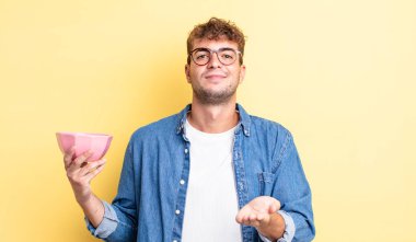 Genç ve yakışıklı bir adam arkadaşça gülümsüyor ve bir konsept sunuyor. boş kase kavramı