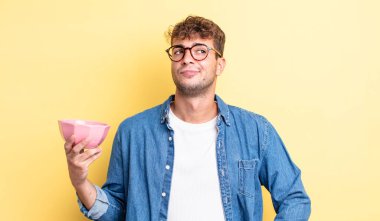 Genç yakışıklı adam omuz silkiyor, kafası karışık ve kararsız. boş kase kavramı