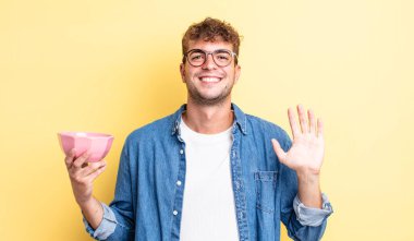 Genç yakışıklı adam mutlu bir şekilde gülümsüyor, el sallıyor, sizi selamlıyor ve selamlıyor. boş kase kavramı