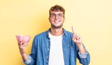 Genç yakışıklı adam gülümsüyor ve arkadaş canlısı görünüyor, bir numarayı gösteriyor. boş kase kavramı