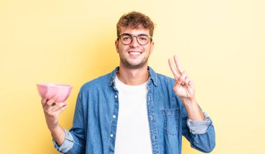 Genç yakışıklı adam gülümsüyor ve arkadaş canlısı görünüyor, iki numarayı gösteriyor. boş kase kavramı