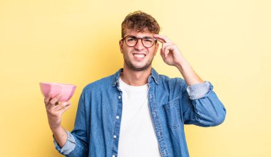 Genç yakışıklı adam kafası karışık ve şaşkın hissediyor, deli olduğunu gösteriyor. boş kase kavramı