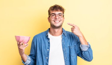 Genç ve yakışıklı bir adam kendi gülüşünü işaret ederek kendine güvenerek gülümsüyor. boş kase kavramı