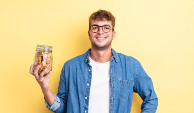 Genç yakışıklı adam mutlu bir şekilde gülümsüyor, eli kalçasında ve kendinden emin. kurabiye şişesi konsepti