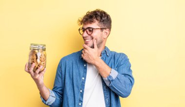 Genç ve yakışıklı bir adam mutlu ve kendinden emin bir ifadeyle gülümsüyor, elleri çenesinde. kurabiye şişesi konsepti