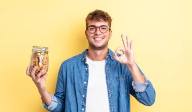 Genç yakışıklı adam kendini mutlu hissediyor, iyi bir jestle onaylıyor. kurabiye şişesi konsepti