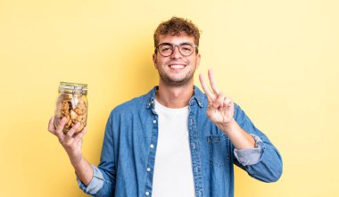 Genç yakışıklı adam gülümsüyor ve mutlu görünüyor, zafer ya da barış işareti yapıyor. kurabiye şişesi konsepti