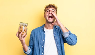 Genç yakışıklı adam mutlu hissediyor, elleri ağzının kenarında bağırıyor. kurabiye şişesi konsepti