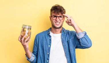 Genç yakışıklı adam kafası karışık ve şaşkın hissediyor, deli olduğunu gösteriyor. kurabiye şişesi konsepti