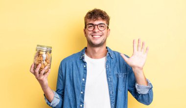 Genç yakışıklı adam mutlu bir şekilde gülümsüyor, el sallıyor, sizi selamlıyor ve selamlıyor. kurabiye şişesi konsepti