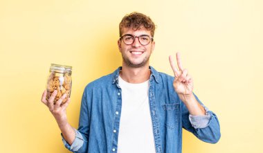 Genç yakışıklı adam gülümsüyor ve arkadaş canlısı görünüyor, iki numarayı gösteriyor. kurabiye şişesi konsepti