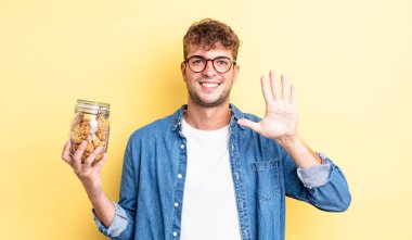 Genç yakışıklı adam gülümsüyor ve arkadaş canlısı görünüyor, beş numarayı gösteriyor. kurabiye şişesi konsepti