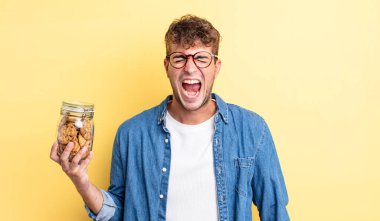 Genç yakışıklı adam agresif bir şekilde bağırıyor, çok kızgın görünüyor. kurabiye şişesi konsepti