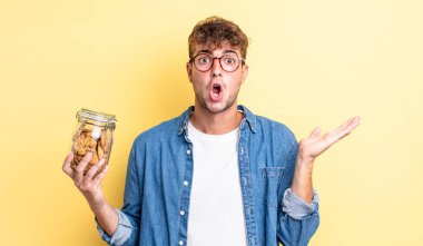 Genç, yakışıklı adam şaşırmış ve şok olmuş görünüyor. Çenesi düşmüş, elinde bir nesne var. kurabiye şişesi konsepti