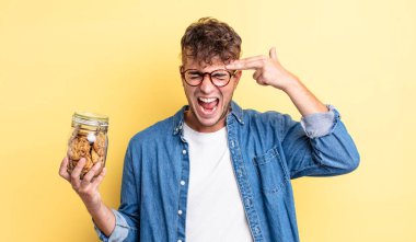 Genç yakışıklı adam mutsuz ve stresli görünüyor, intihar jesti silah işareti yapıyor. kurabiye şişesi konsepti