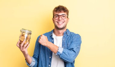 Genç yakışıklı adam kendini mutlu hissediyor ve bir meydan okumayla yüzleşiyor ya da kutluyor. kurabiye şişesi konsepti