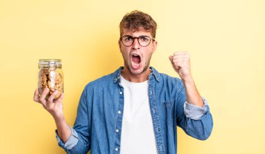 Genç yakışıklı adam sinirli bir ifadeyle agresif bir şekilde bağırıyor. kurabiye şişesi konsepti