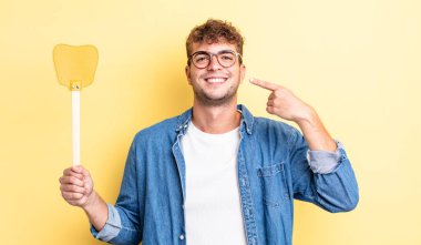 Genç ve yakışıklı bir adam kendi gülüşünü işaret ederek kendine güvenerek gülümsüyor. Sineklik konsepti