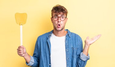 Genç, yakışıklı adam şaşırmış ve şok olmuş görünüyor. Çenesi düşmüş, elinde bir nesne var. Sineklik konsepti